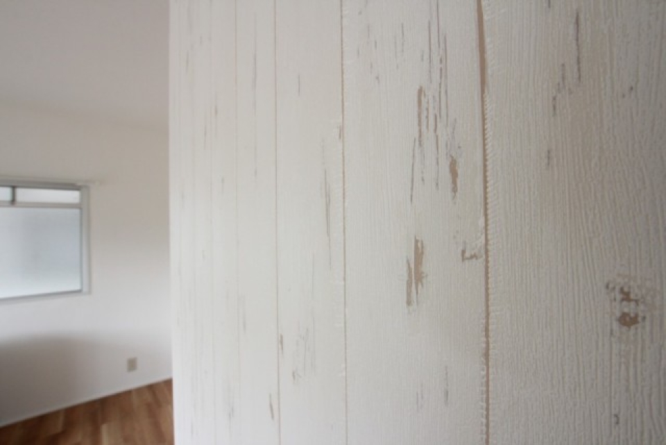 白いペンキ塗りの板材のようなプリントがされた壁紙がこの部屋の主役