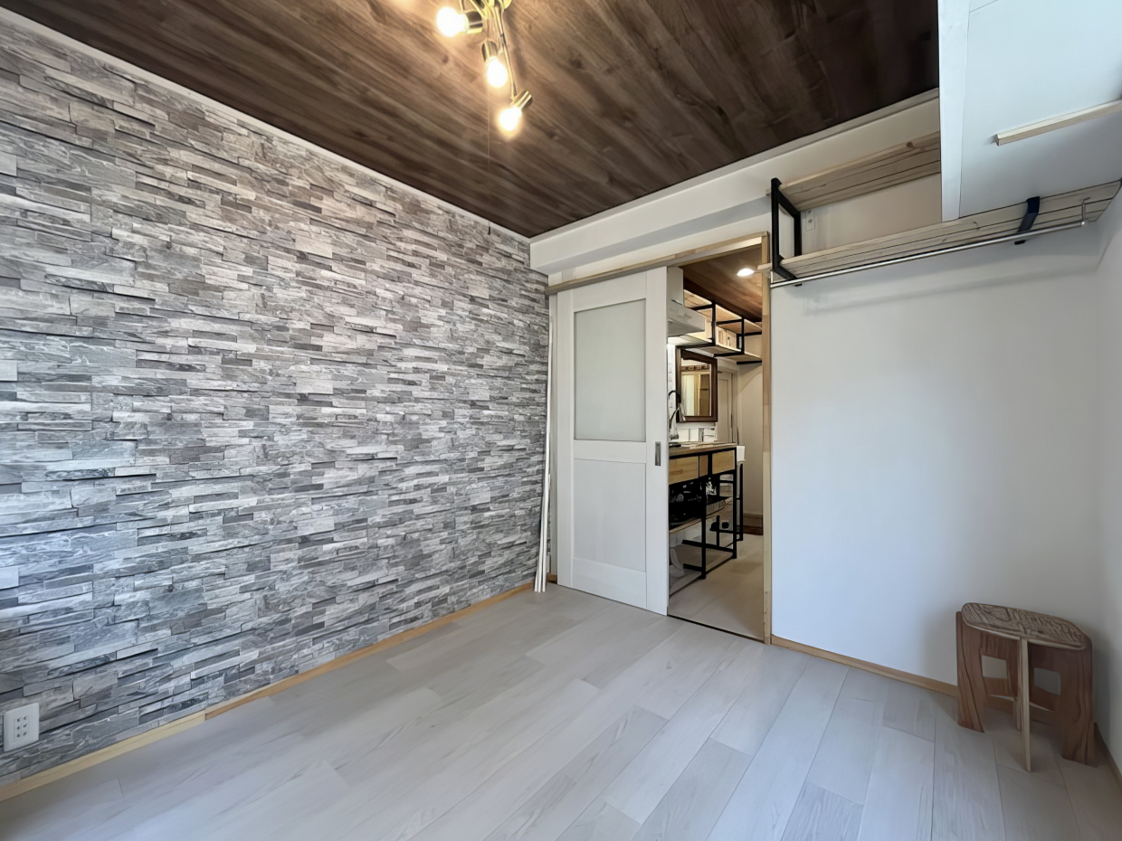 存在感抜群のグレーの石目柄の壁紙を、ダークブラウンの天井とゴールドのライトが落ち着かせている感じ